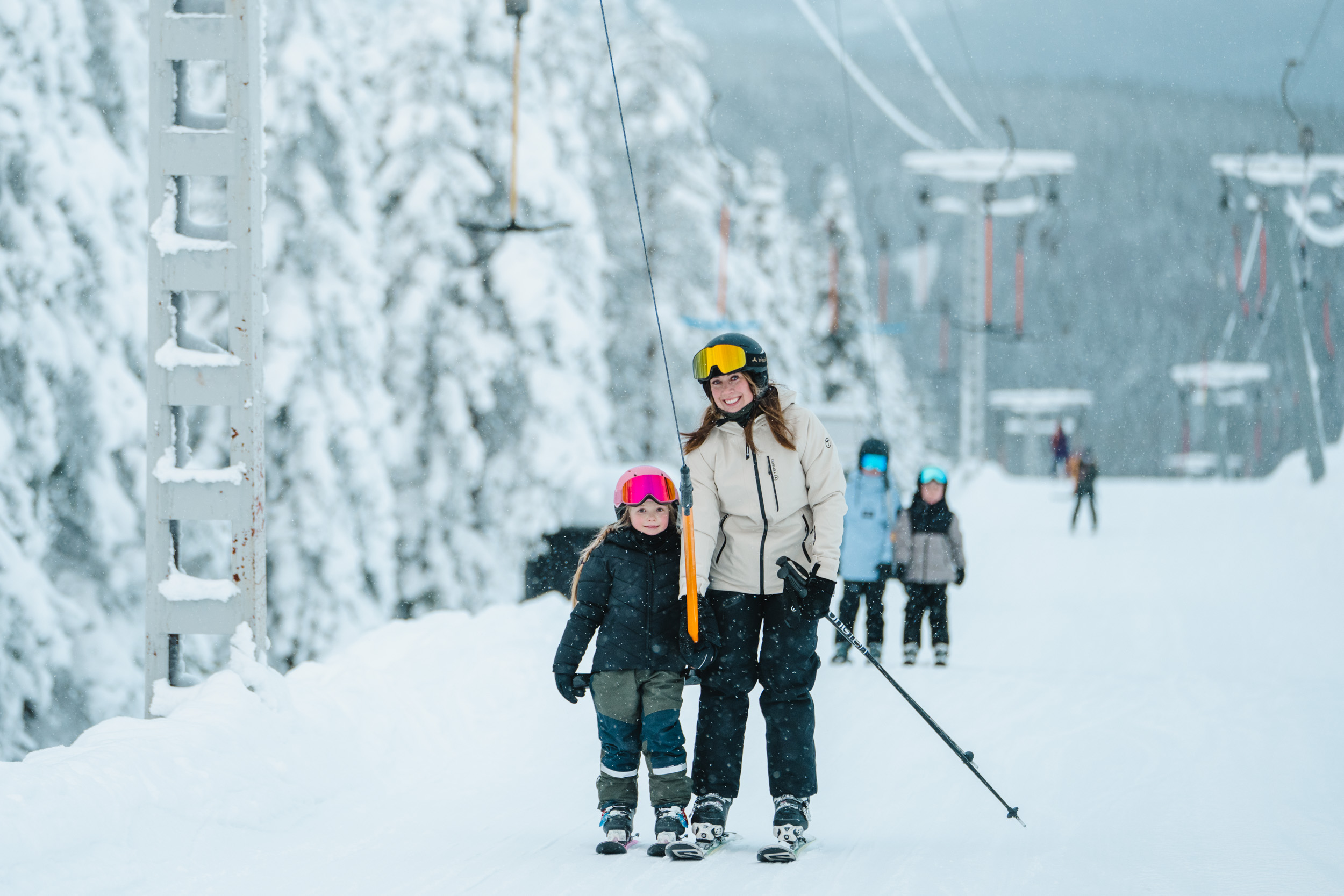 Vuxen och barn med skidor vid lift i snötäckt backe